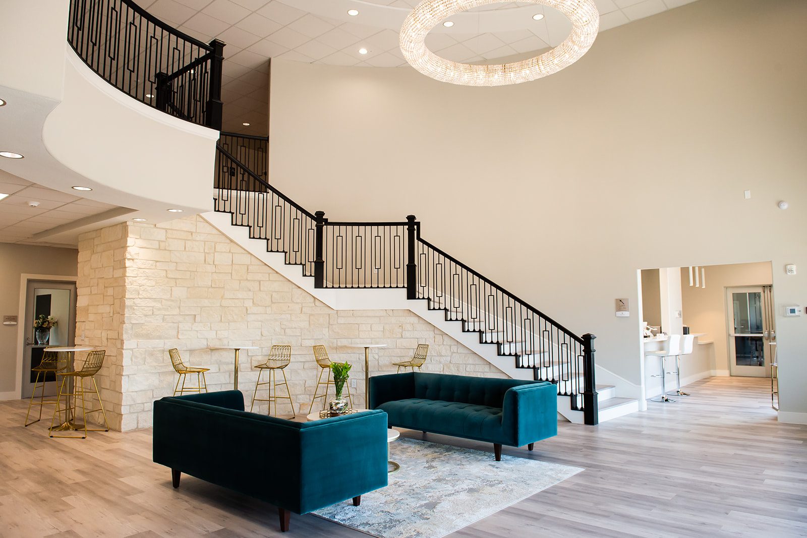 Bellevana two-story lobby with curved staircase, ring crystal chandelier, teal velvet sofas, and stone accent wall